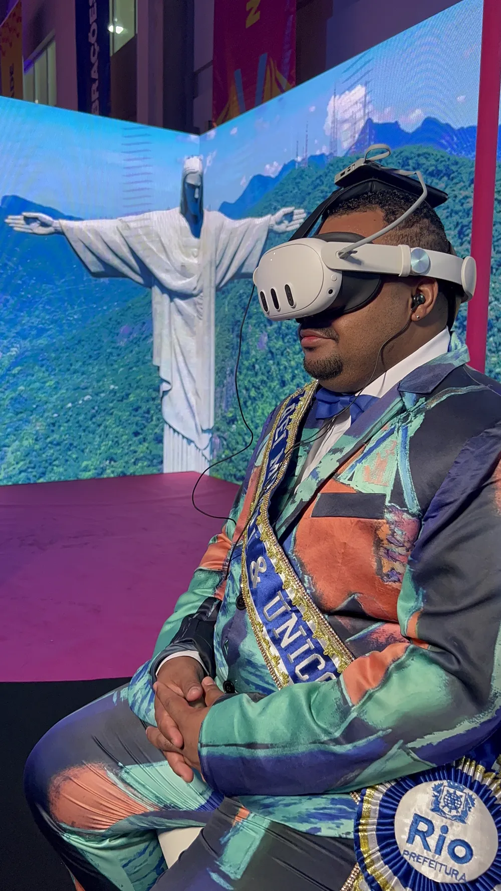 Folião fantasiado usando óculos VR diante de um telão com o Cristo Redentor